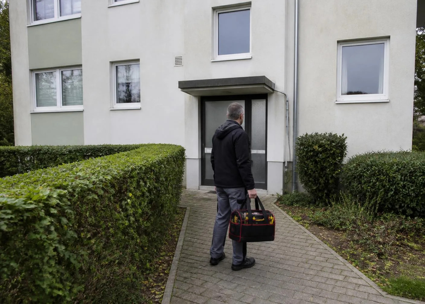 Hausmeister mit Werkzeugtasche am Eingang einer gepflegten Wohnanlage